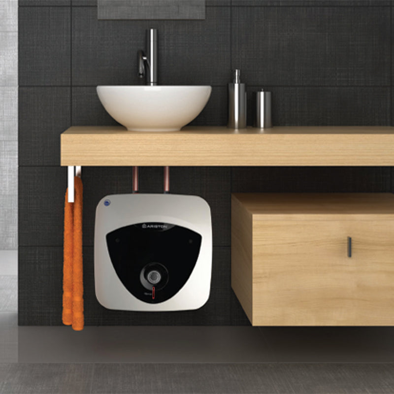 A wall-mounted bathroom water heater in a white and black oval design, installed beneath a light wood vanity shelf in a modern bathroom setting with a white bowl sink and dark tiled wall.