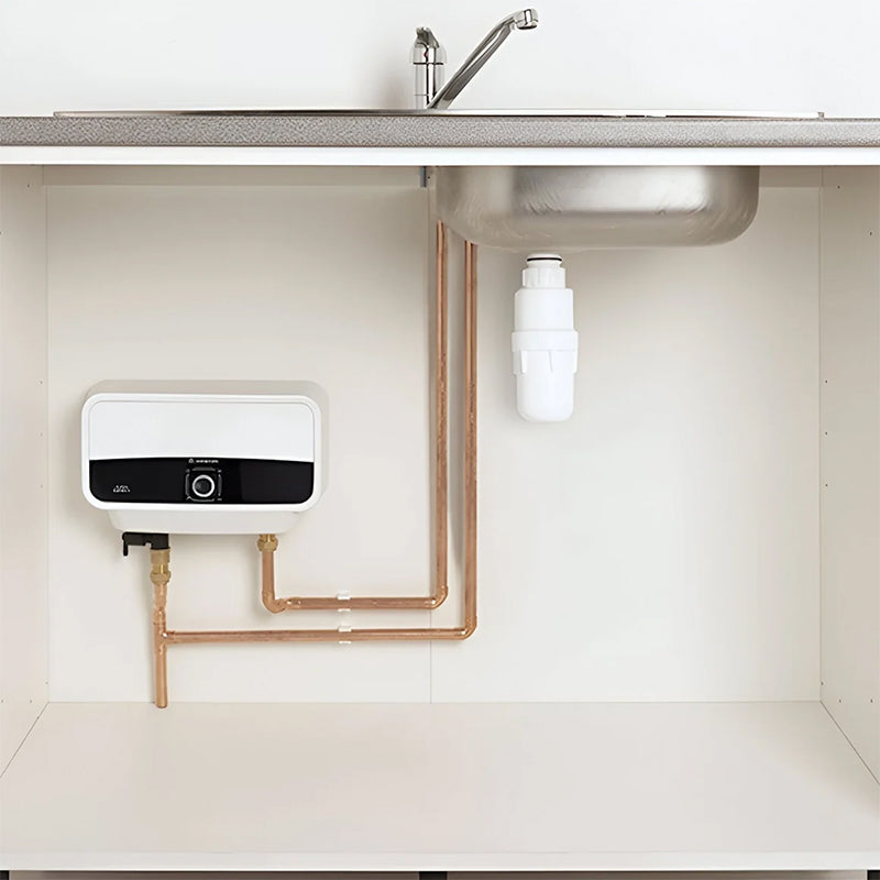 Water heater and pipes under a kitchen sink with a white tiled wall.