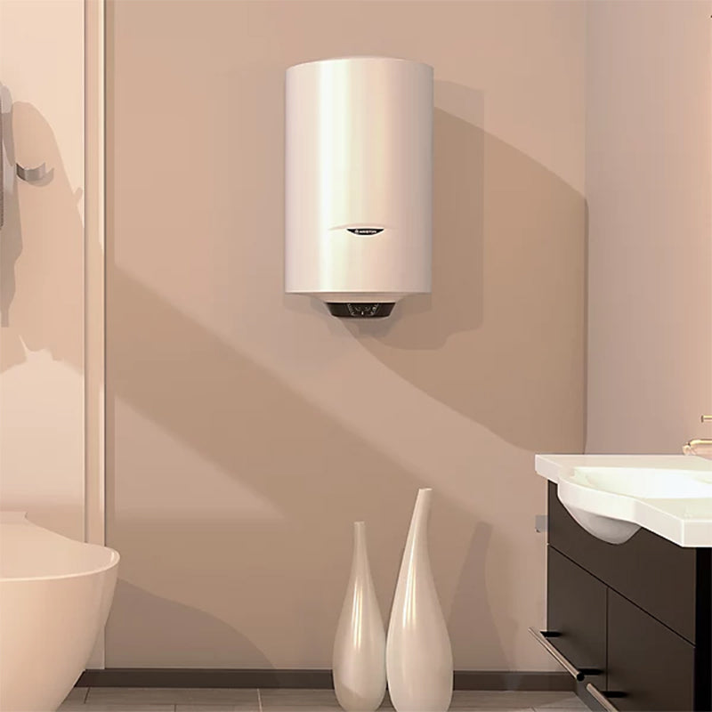 A white cylindrical wall-mounted water heater installed on a beige wall in a modern bathroom setting, with a sink, dark cabinet, and two white decorative vases below.